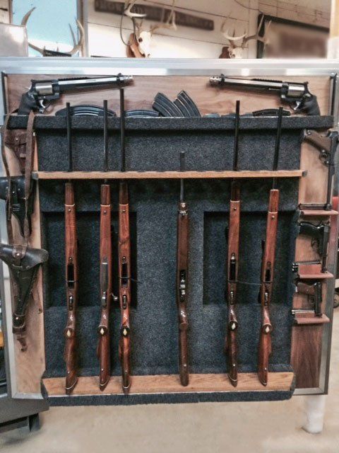 Wooden rifle rack holding several long guns with black stocks and barrels in a workshop setting