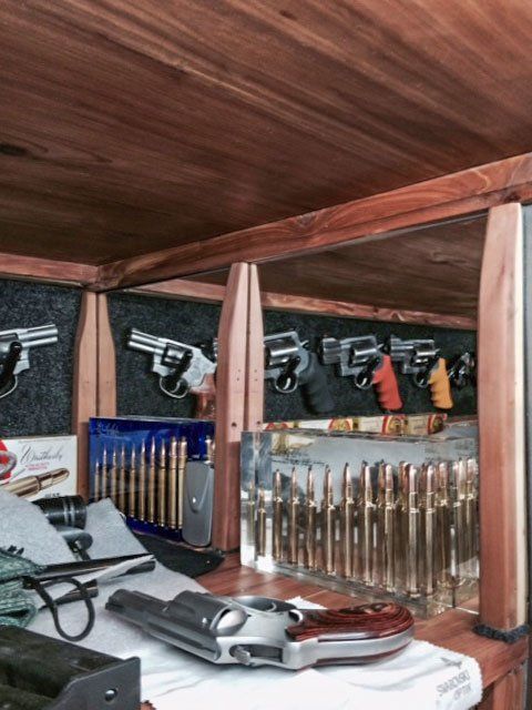 Gun display case with pistols, revolvers, and rifle cartridges on shelves and a wooden ceiling