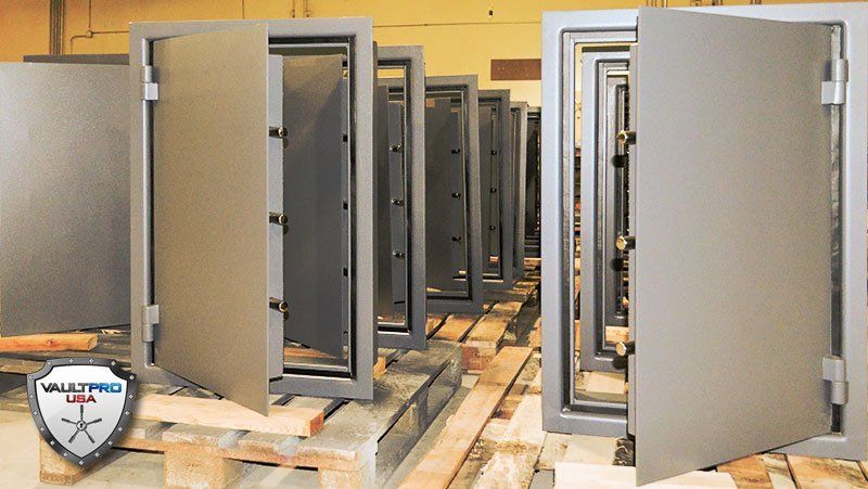 Rows of open gray metal safes or vault doors on wooden pallets in a warehouse.
