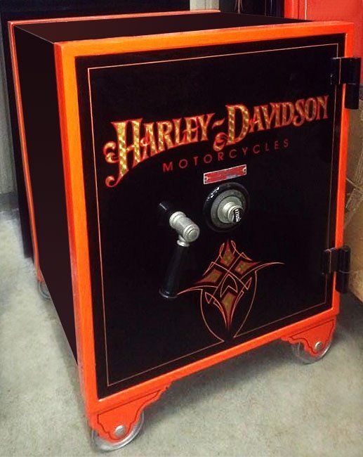 Black Harley-Davidson safe with orange trim and red wheels on a carpeted floor