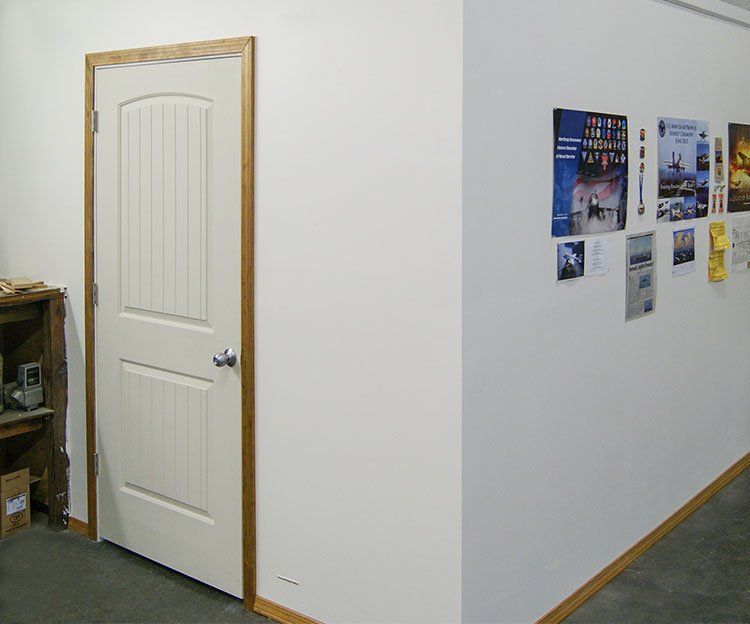 Hallway corner with white door, wood trim, and posters on a blank white wall