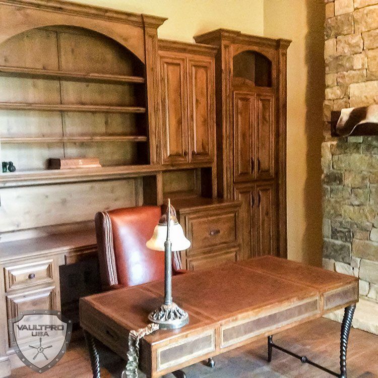 Wood-paneled office with built-in cabinets, wooden desk, leather chair, and stone fireplace