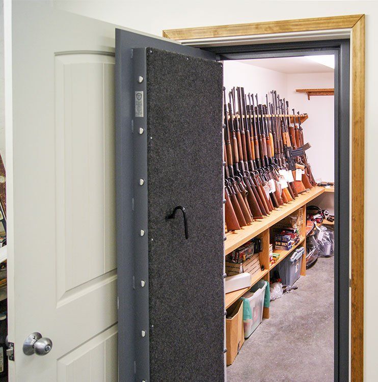 Open gun safe filled with rifles and firearms on wooden shelves inside a room