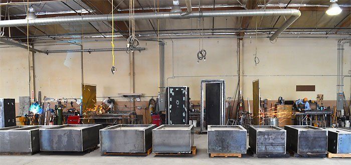 Warehouse with rows of large industrial bins and machines under exposed ceiling pipes