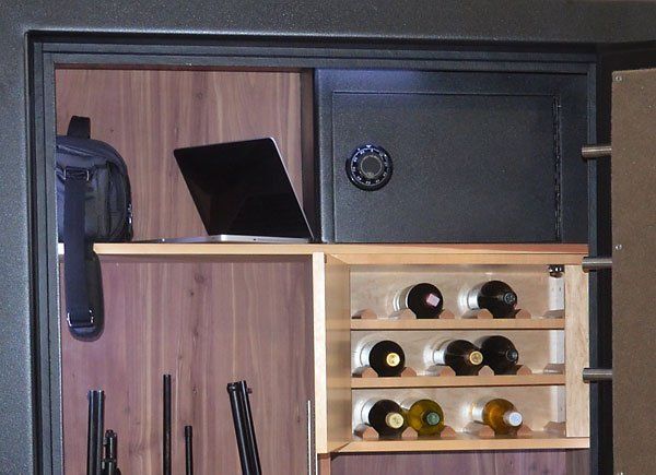 Built-in cabinet with wooden shelves, wine bottles, a black laptop, and a dark safe door.