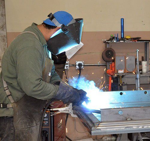 Welder in blue helmet welding metal in a workshop, bright arc light and sparks visible