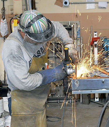 Worker using a grinder, sending sparks across a metal workbench in a workshop