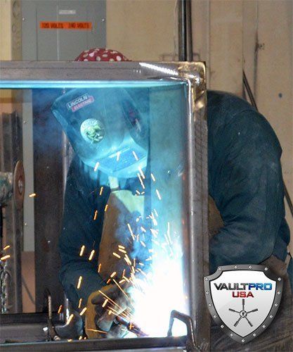 Welder in blue jacket and face shield welding metal frame, sparks flying in workshop.