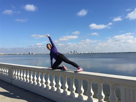 A woman is kneeling on a railing overlooking a body of water.