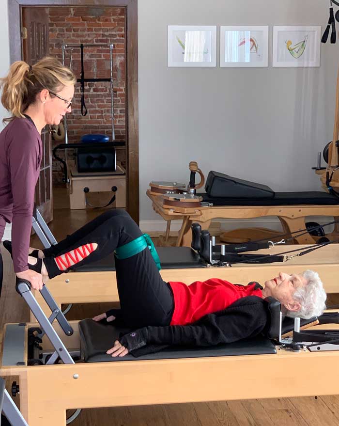 A woman is teaching an older woman how to do pilates on a pilates refomer.