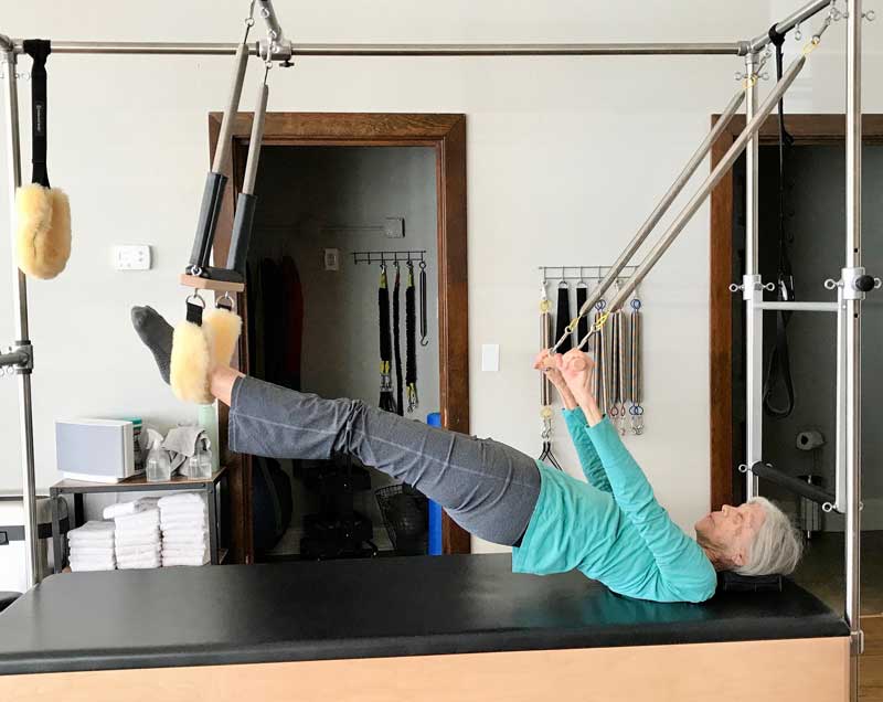 A woman is laying on a pilates machine with her legs up.