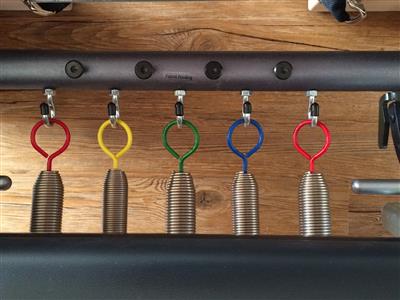 A bunch of springs are hanging from a metal bar on a wooden floor.