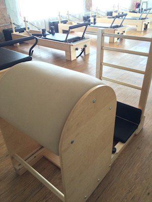 A wooden chair is sitting on a wooden floor in a pilates studio.