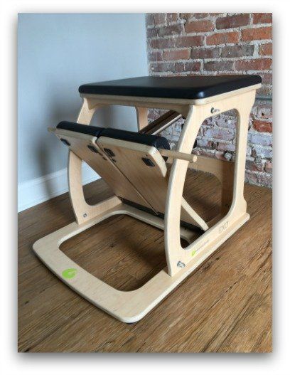 A wooden pilates chair sits on a wooden floor in front of a brick wall
