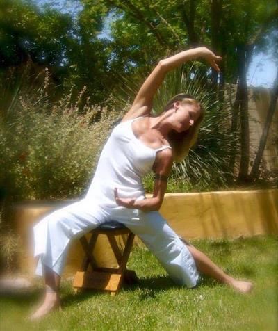 A woman is doing a yoga pose while sitting on a stool in the grass