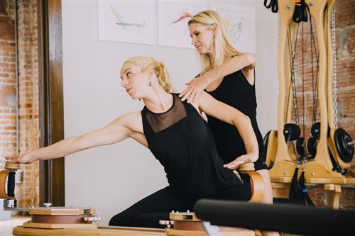 A woman is helping another woman do exercises on a pilates machine.