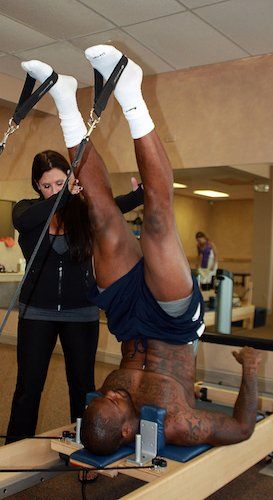 A man is doing exercises on a pilates machine while a woman watches.