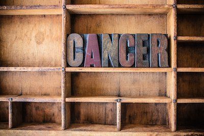 The word cancer is written in wooden letterpress type on a wooden shelf.