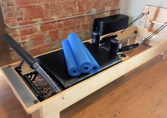 A wooden pilates reformer with blue yoga mats on top of it.
