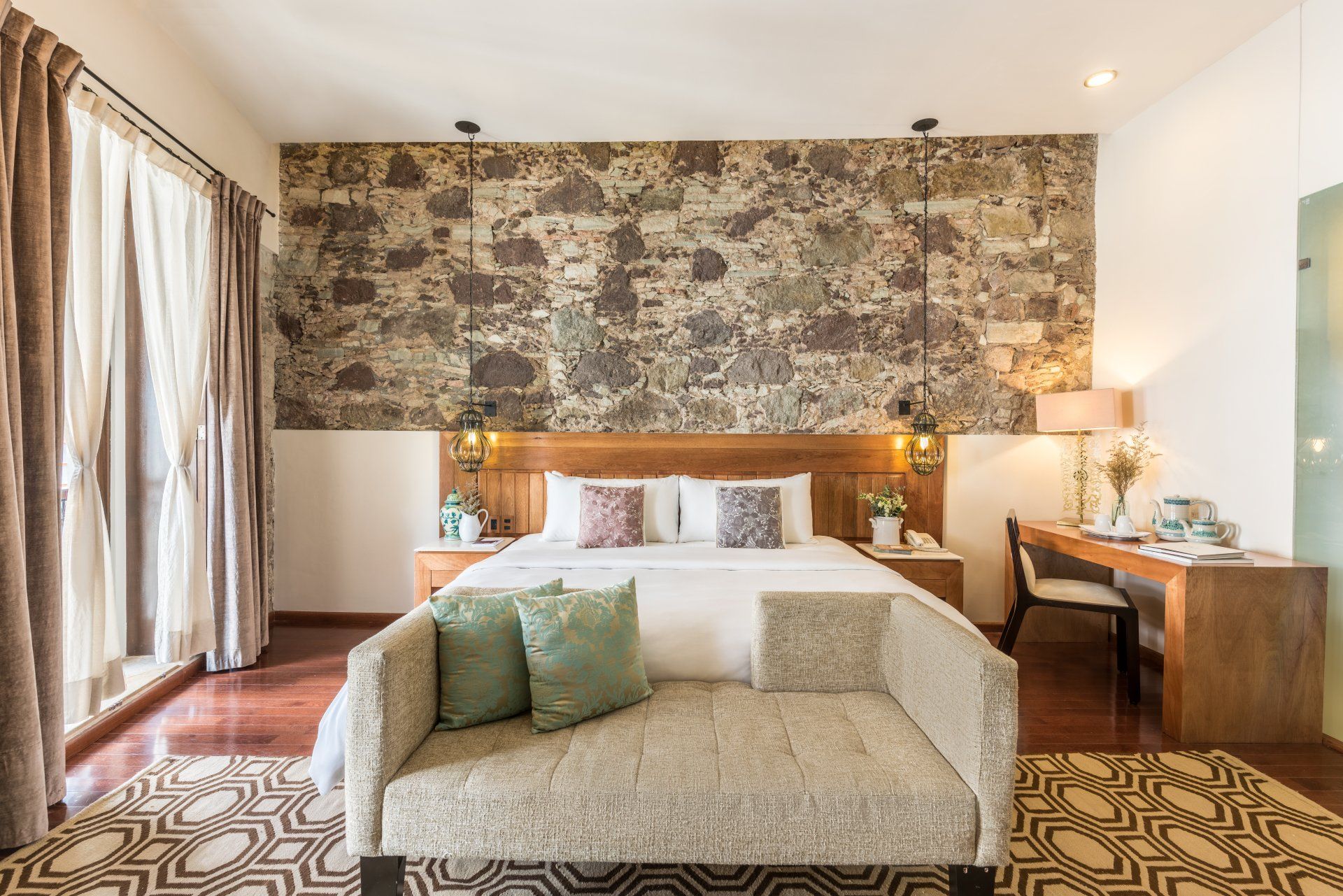 Cozy bedroom with patterned wallpaper, upholstered bench, warm lighting, and curtains by large windows