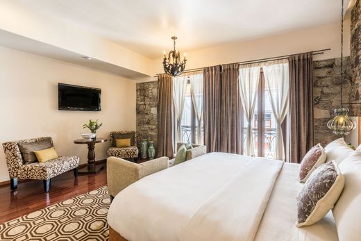 Elegant bedroom with bed, chandelier, wall TV, patterned rug, and large window drapes