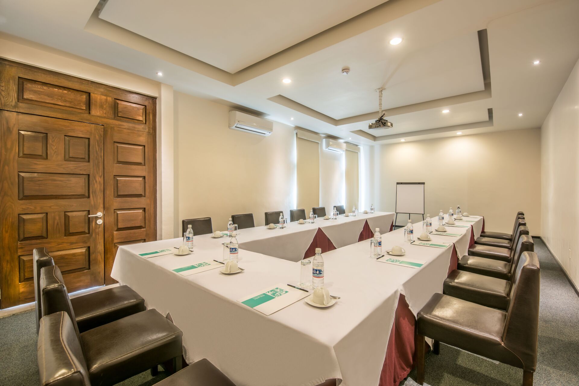 Empty conference room with U-shaped table, brown leather chairs, and cream walls with recessed lighting.