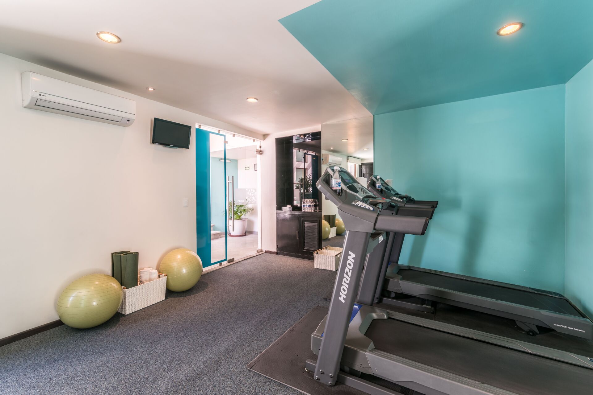 Modern gym room with treadmills, exercise balls, and turquoise walls
