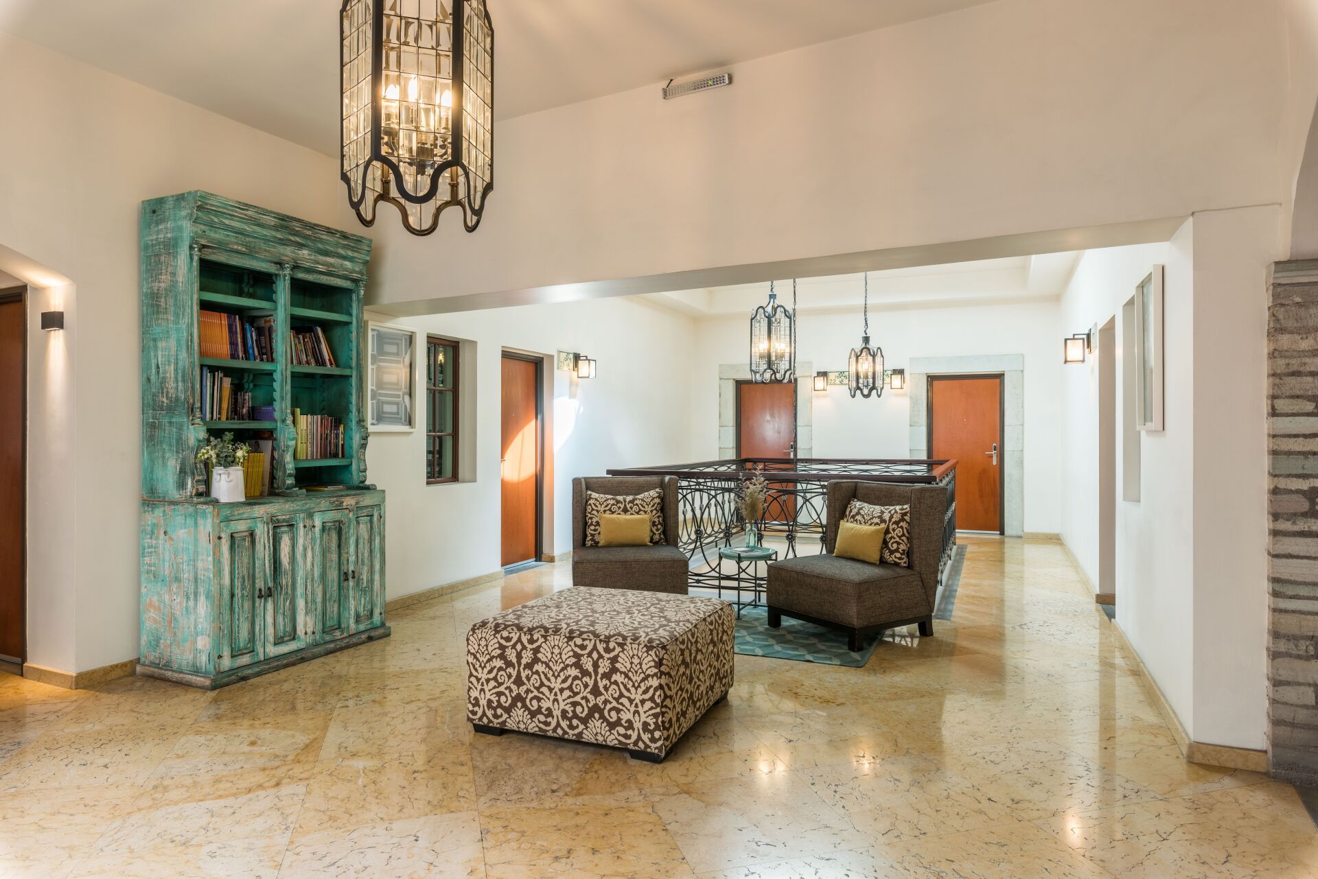 Spacious living room with turquoise cabinet, brown sectional, and patterned ottoman under hanging chandeliers