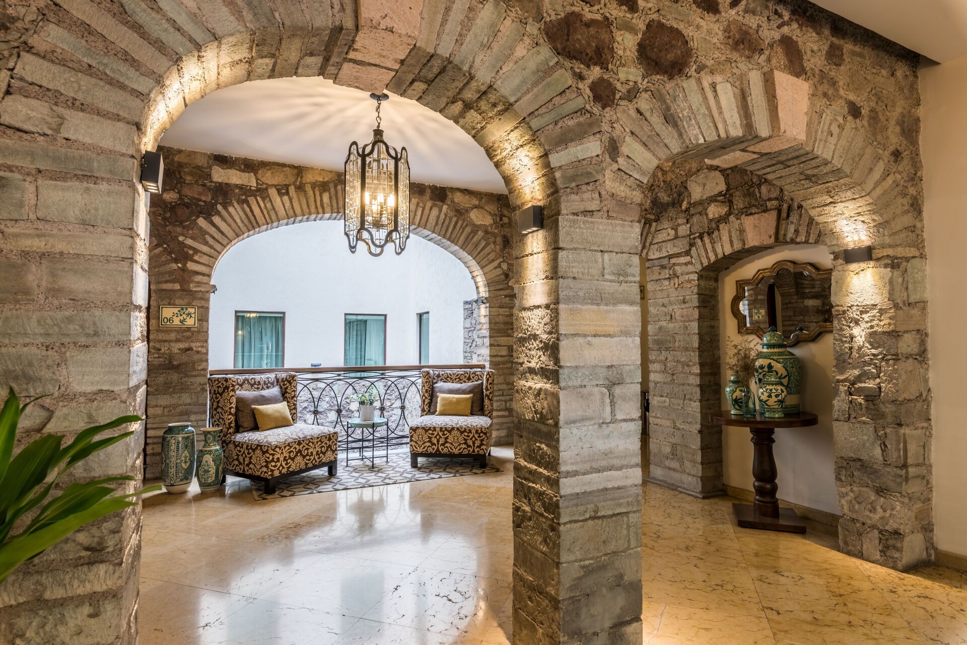 Stone arched hallway opening to a bright seating area with patterned sofas and a hanging lantern