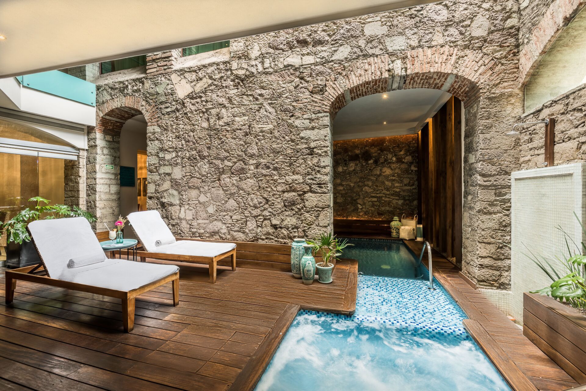 Stone courtyard spa with lounge chairs and a small pool under an arched doorway