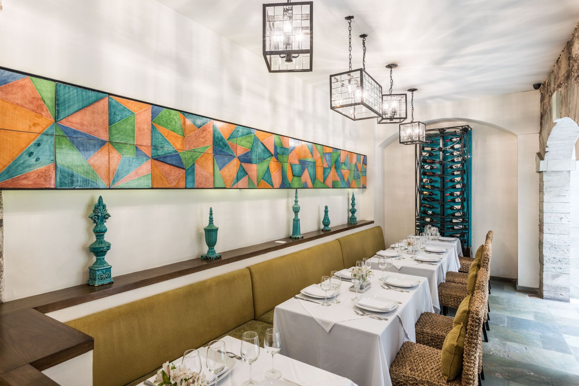 Stylish restaurant dining room with long white table settings, patterned wall art, and wicker chairs