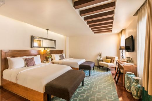 Hotel room with two twin beds, patterned rug, desk, TV, and warm wood ceiling beams