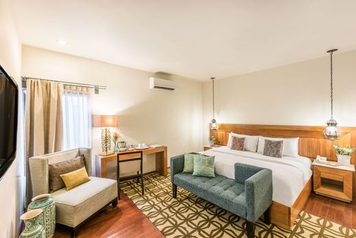 Modern hotel room with a bed, teal sofa, desk, armchair, and warm lighting