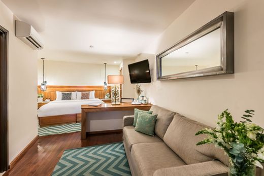 Hotel room with bed, sofa, desk, wall-mounted TV, and mirror in a warm-toned interior