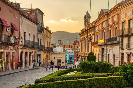Sunset over a cobblestone street with colorful historic buildings and a few pedestrians