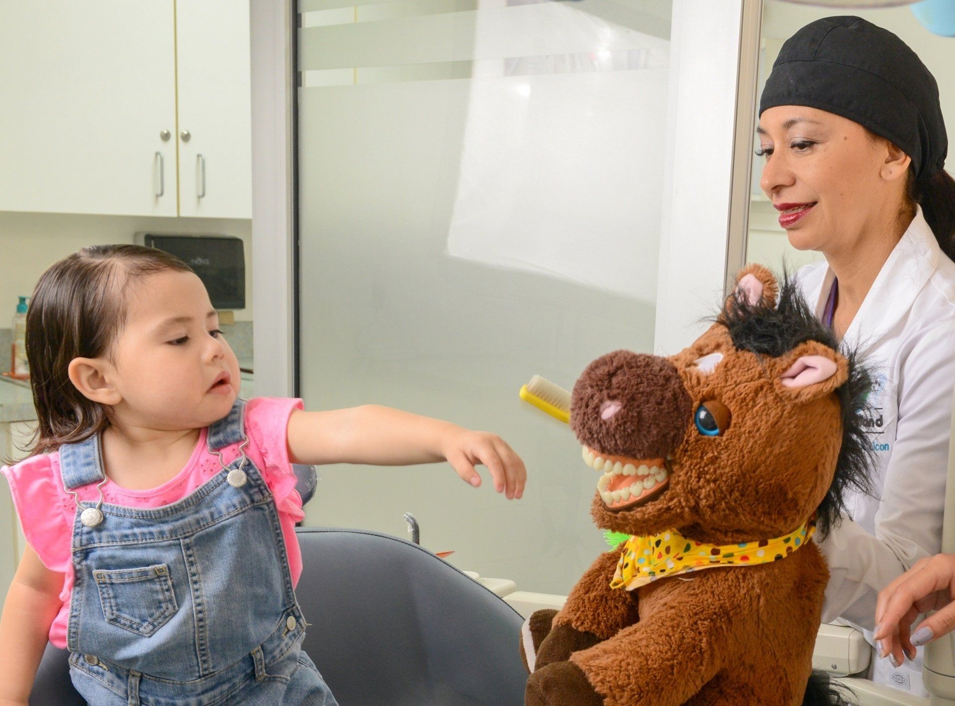 A little girl is brushing her teeth with a stuffed horse.