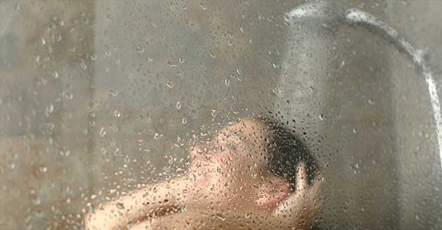 a man is taking a shower behind a glass door .