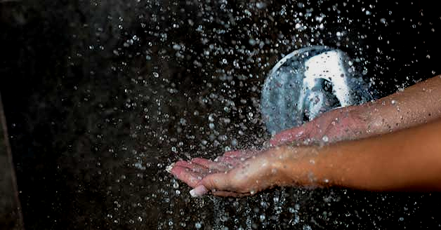 a woman is taking a shower with her hands in the water .
