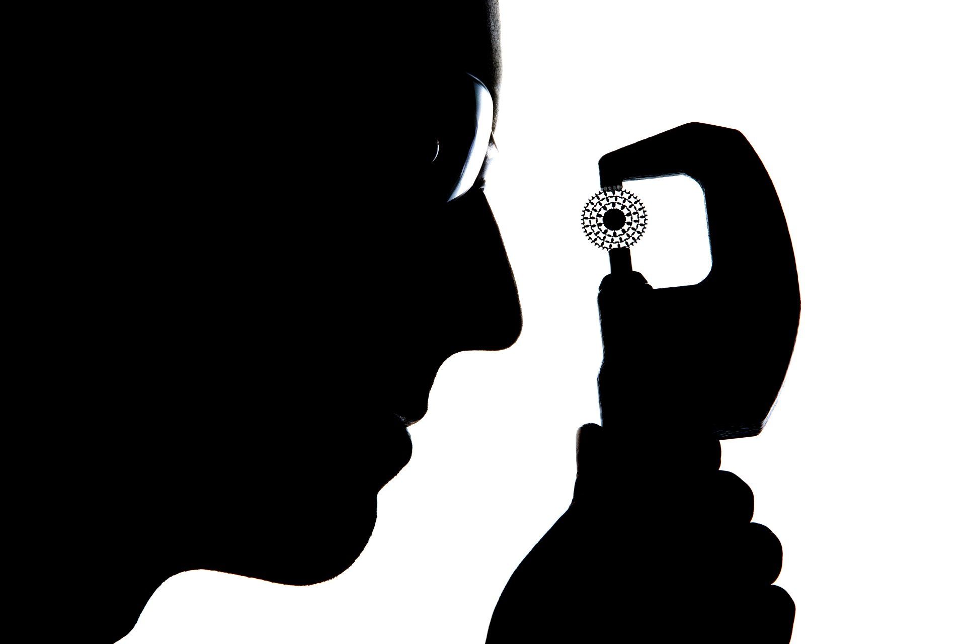 A silhouetted engineer examines technical component up close. 