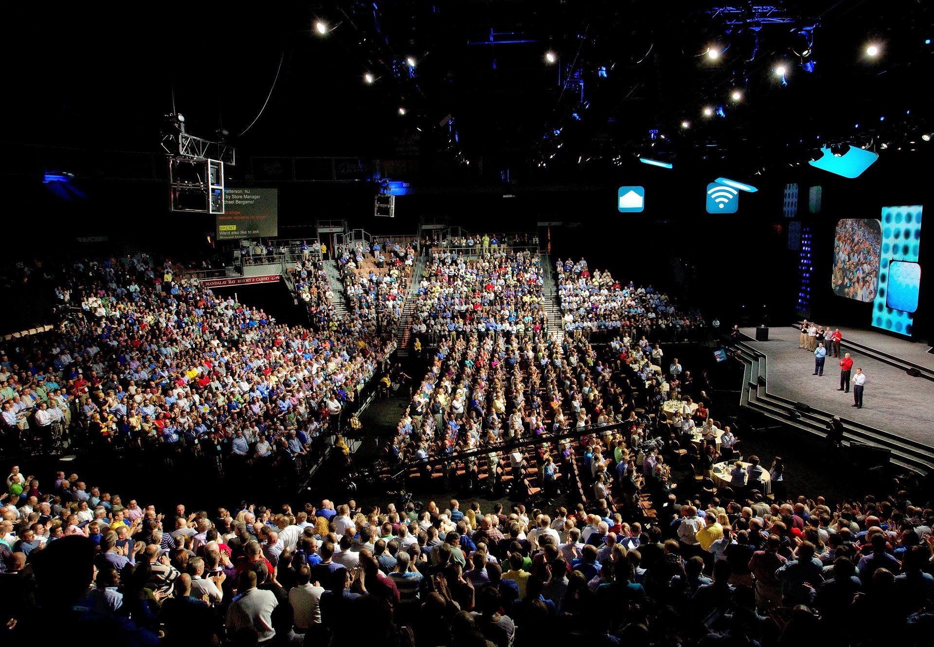 Crowds of employees applaud speakers at a corporate event.