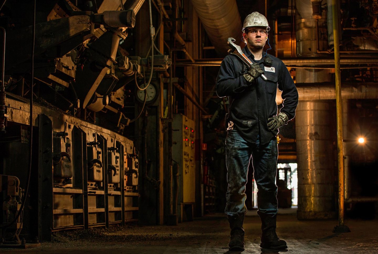 Portrait of manufacturing facility specialist. The man is holding a wrench and has a hand on his hip. He is posing for the camera. He is wearing safety equipment. 