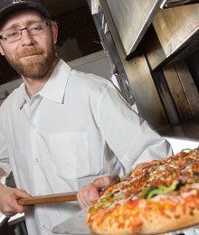 pizza chef getting a fresh pizza out of oven