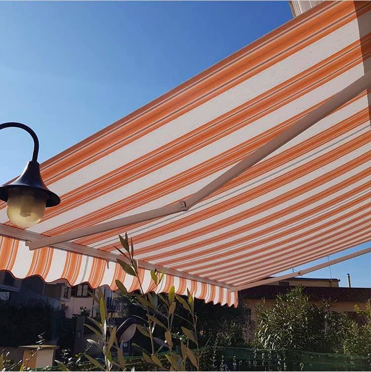 Tenda da sole a strisce arancioni e bianche sopra uno spazio esterno in una giornata di sole.
