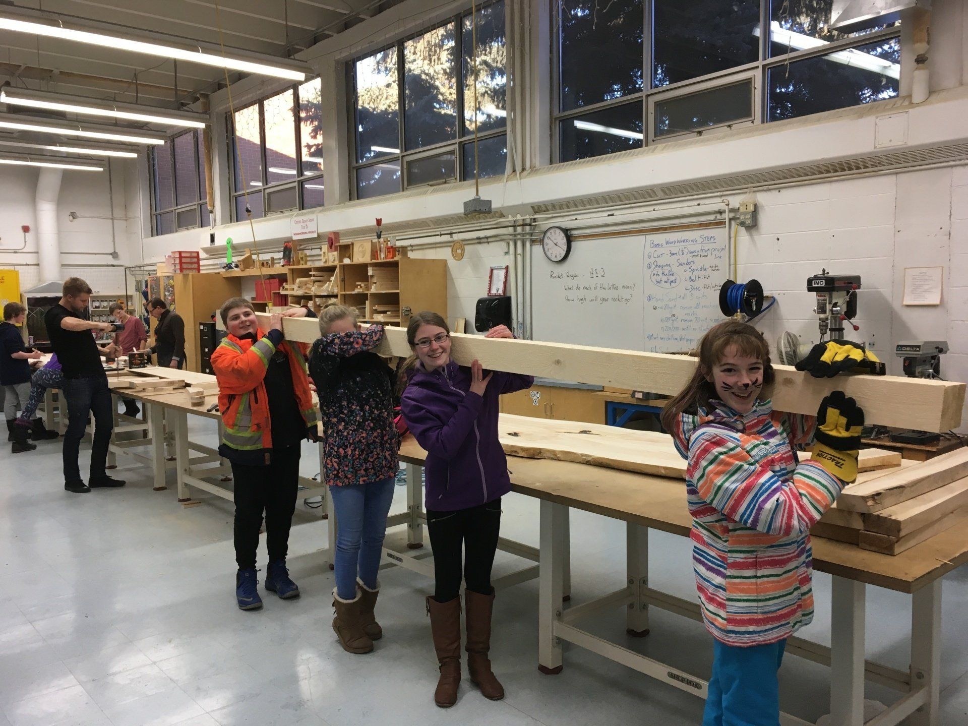 Children working at a long workshop bench in a bright classroom, with tools and materials around them.