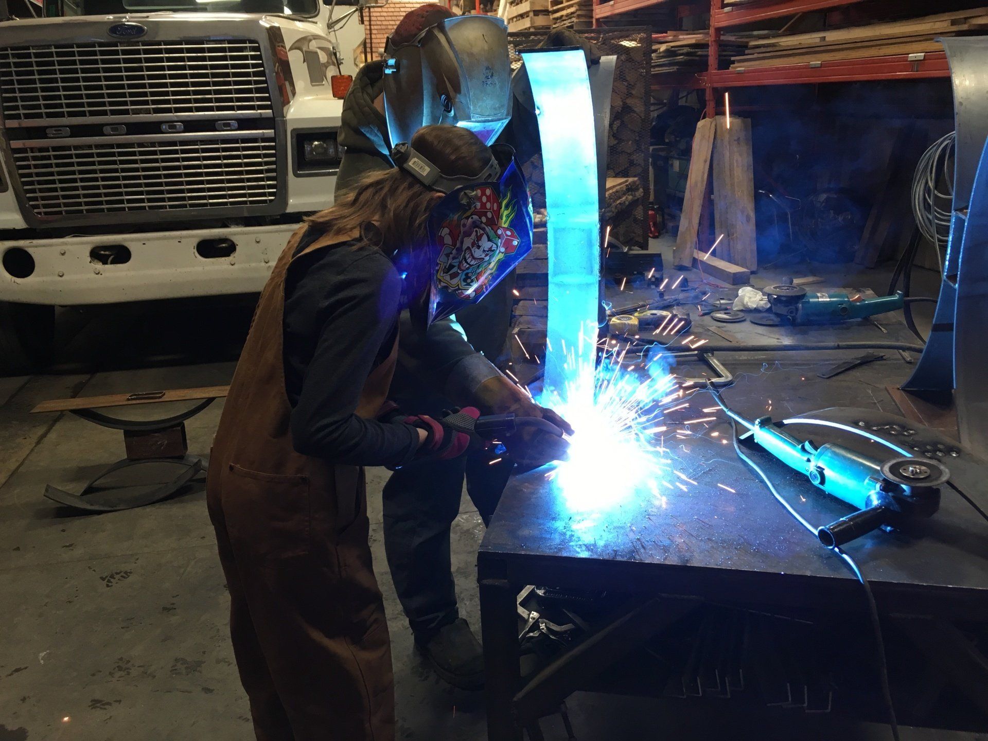 Person welding metal in a workshop, bright blue sparks lighting the scene