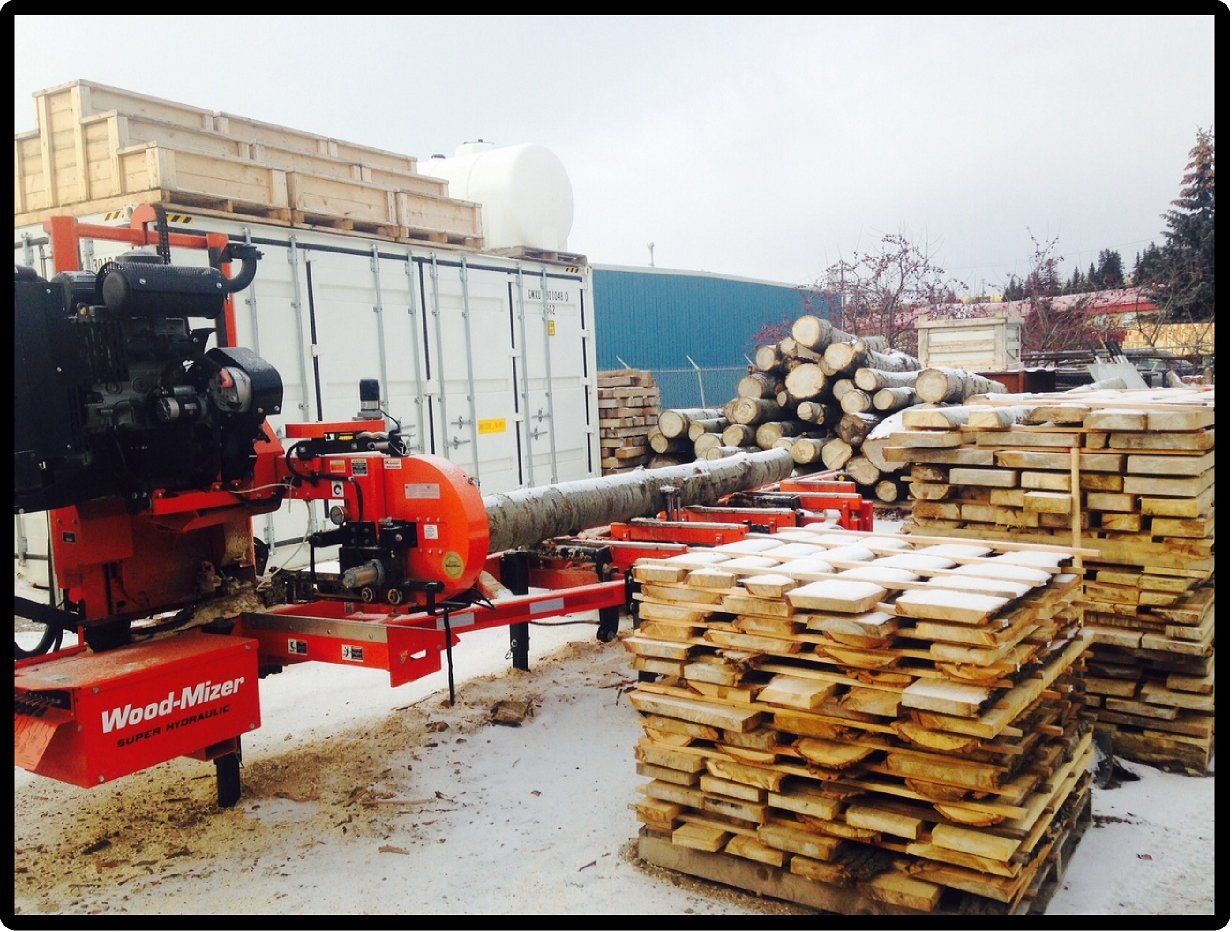 Wood-Mizer sawmill cutting logs beside stacks of lumber at a snowy lumberyard