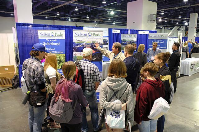 Crowd gathered at a trade show booth with blue banners and display posters