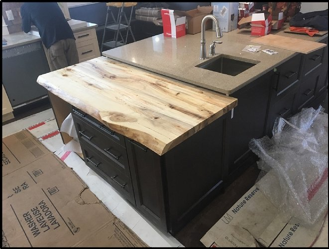 Kitchen island with butcher-block top and stainless sink, surrounded by boxes in a room under renovation