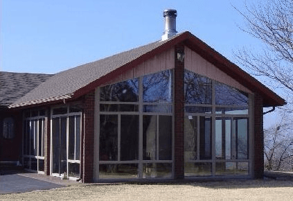 Modern house exterior with large windows, red roof, and tall chimney under a clear blue sky
