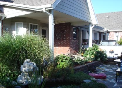 Front porch and garden of a suburban house with shrubs, flowers, and a small stone statue